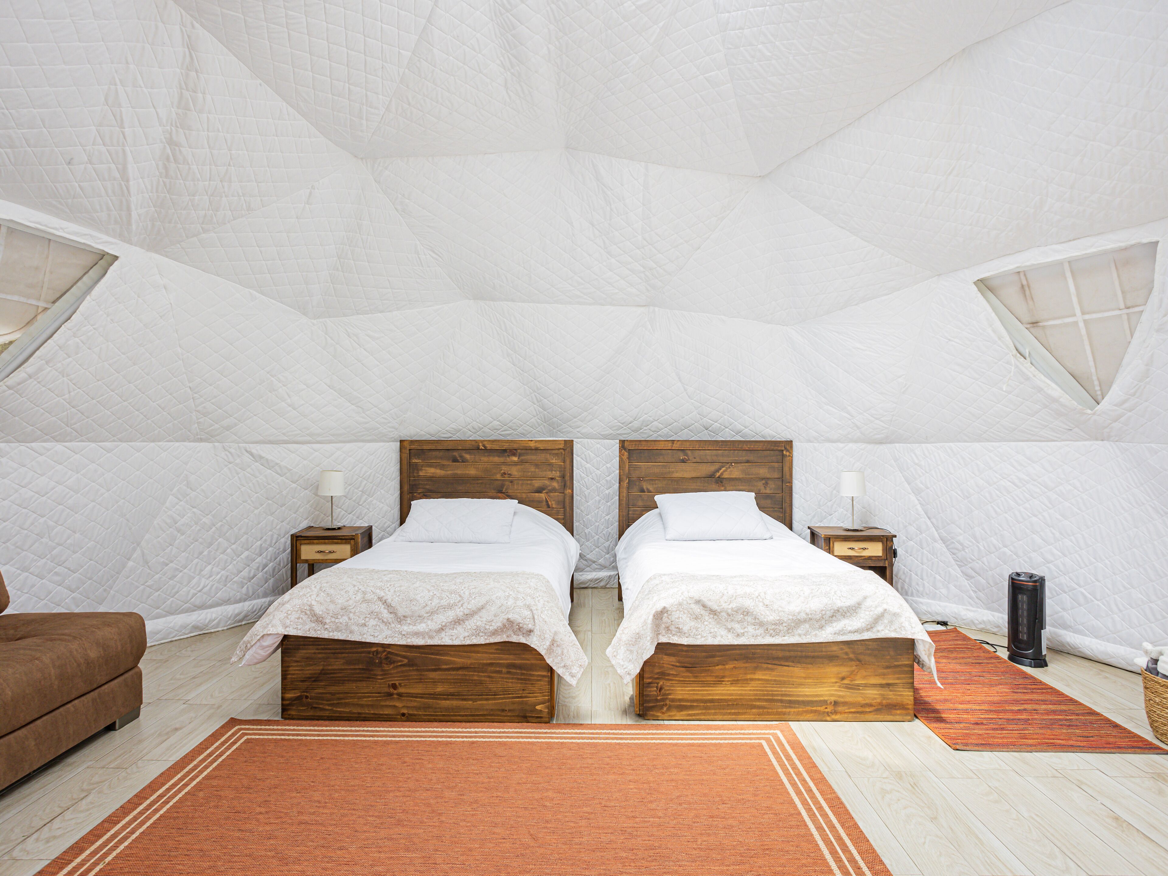 A cozy bedroom with two wooden beds, a brown sofa, and a small table with a lamp.
