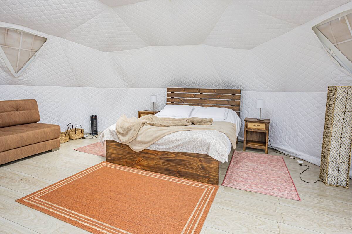 A bedroom with a wooden bed, a brown sofa, and a small bedside table with a lamp.