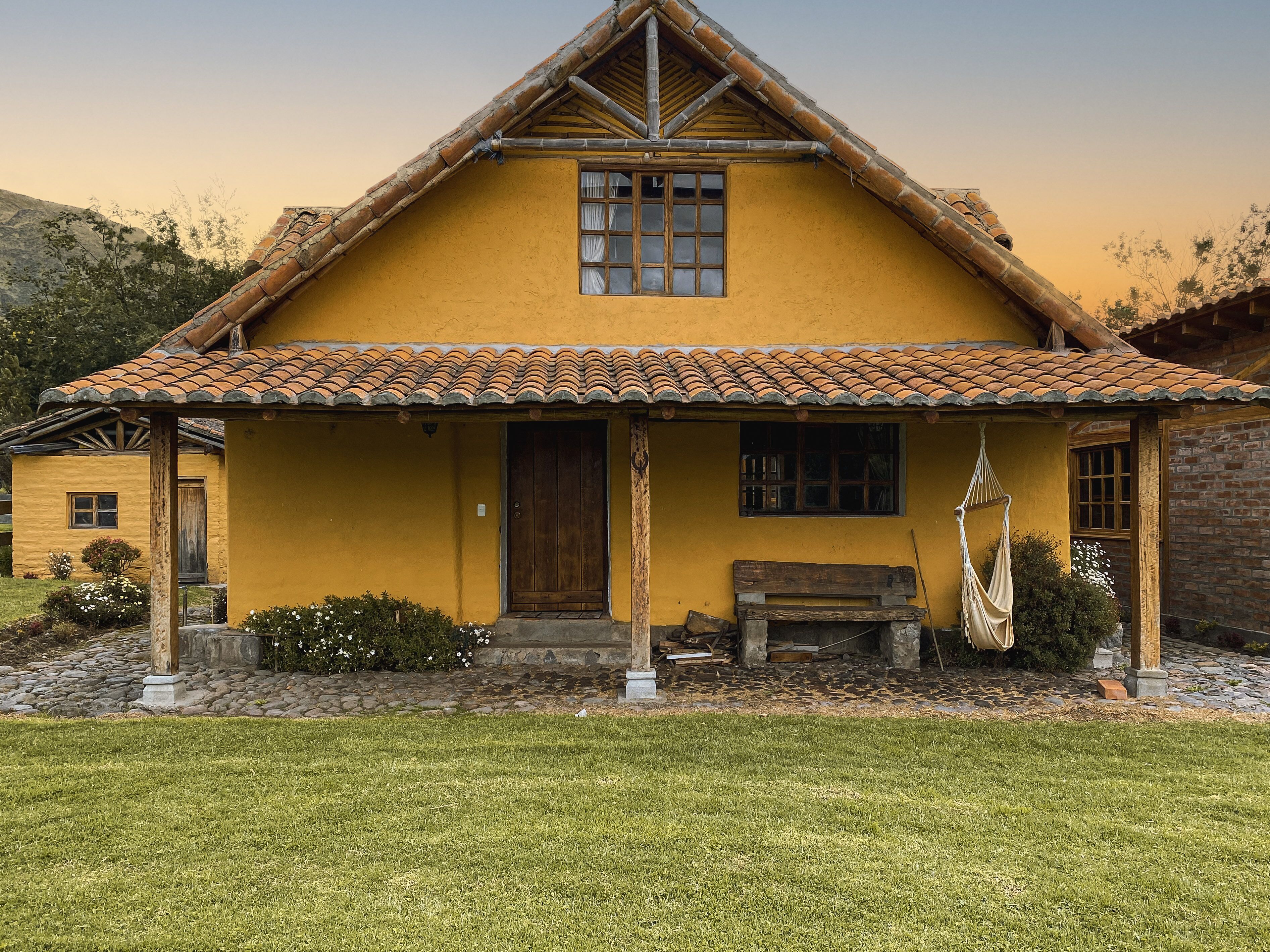 A yellow house with a tiled roof, a wooden door, and a bench outside.