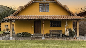 A yellow house with a tiled roof, a wooden door, and a bench outside.
