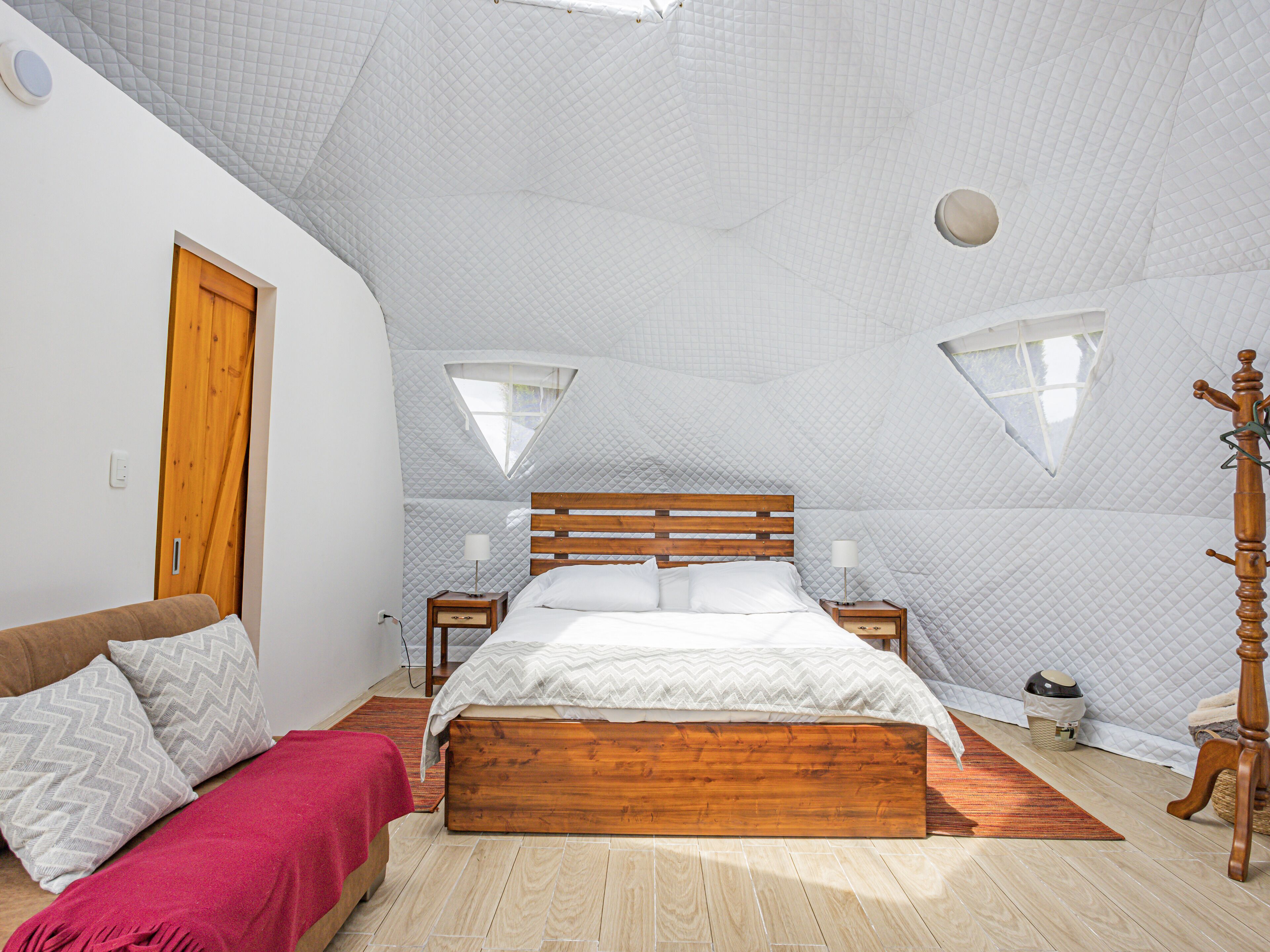 A bedroom with a wooden bed, a wooden wardrobe, a wooden nightstand, a red throw blanket, and a wooden coat stand.