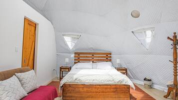 A bedroom with a wooden bed, a wooden wardrobe, a wooden nightstand, a red throw blanket, and a wooden coat stand.