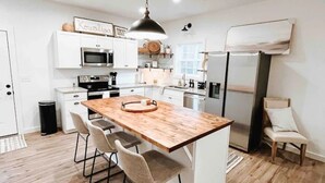 Uma cozinha moderna com ilha de madeira, armários brancos, eletrodomésticos de aço inoxidável e uma luminária pendente.