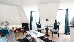 Moderni, avoin pohjainen huoneisto, jossa on korkea katto, sohva, kaksi nojatuolia, sohvapöytä ja ruokapöytä.