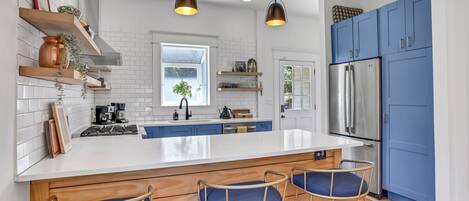 A modern kitchen with a central island, bar stools, blue cabinets, and a stainless steel refrigerator.