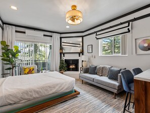 Ein Schlafzimmer mit Bett, einer Couch, einem Schreibtisch, einem Kamin und einem großen Fenster.