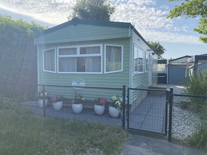 Una casa móvil de un piso con patio delantero cercado, un letrero que dice 'Baysdale' y plantas en macetas.