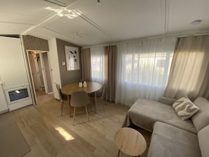 A modern living room with a sofa, a dining table with chairs, a small round table, and a kitchen area with an oven.