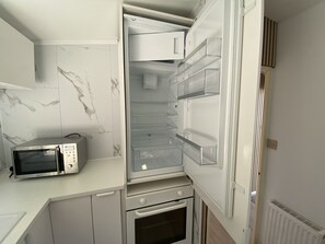 A compact kitchen with a built-in microwave, oven, and a refrigerator with transparent drawers.