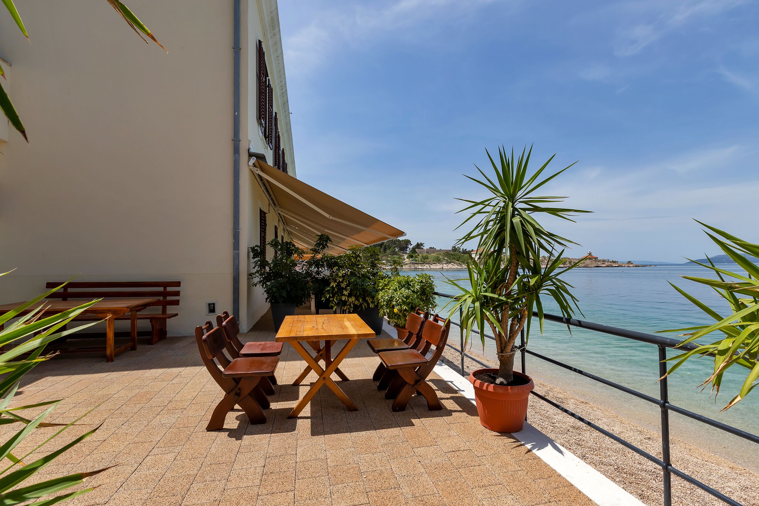 Une terrasse avec une table et des chaises en bois, un pot de fleurs et une vue sur la mer.