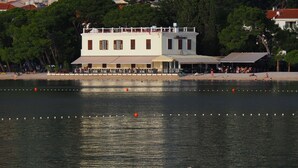 A waterfront building with a balcony, a covered seating area, and a pool with floating barriers. - Beach rooms Riviera (Makarska)