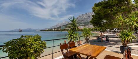 A wooden table and chairs on a terrace with a view of the sea and mountains.