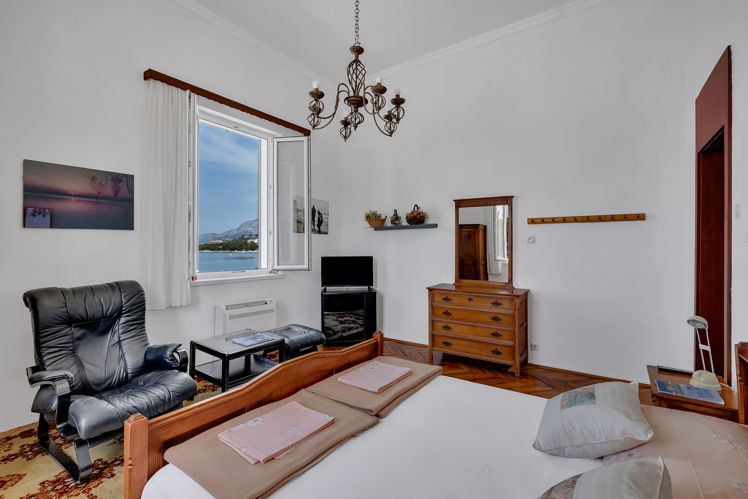 A bedroom with a bed, a chair, a dresser, a television, and a window with a view of mountains.