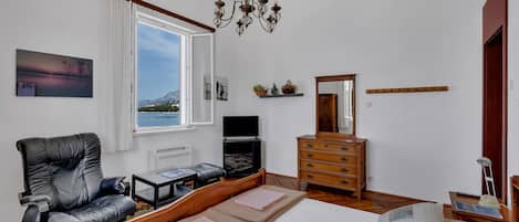 A bedroom with a bed, a chair, a dresser, a television, and a window with a view of mountains.