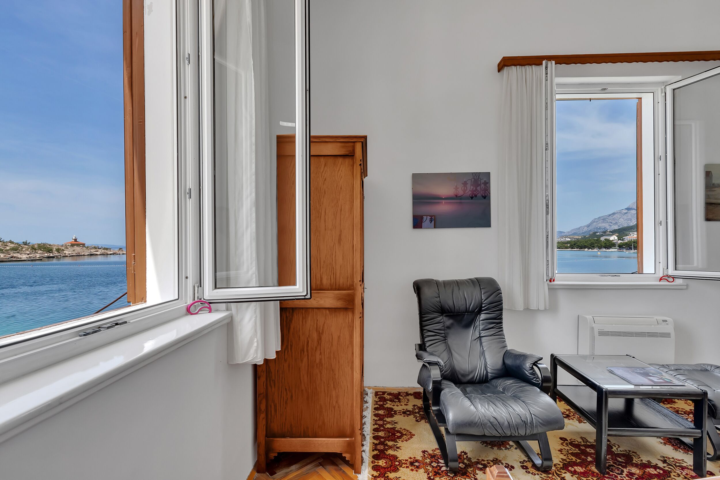 A room with a view of the sea, a wooden door, a black leather chair, and a small table.