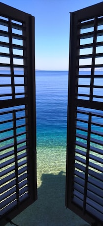 A view through open wooden shutters to a clear blue sea with visible underwater terrain.