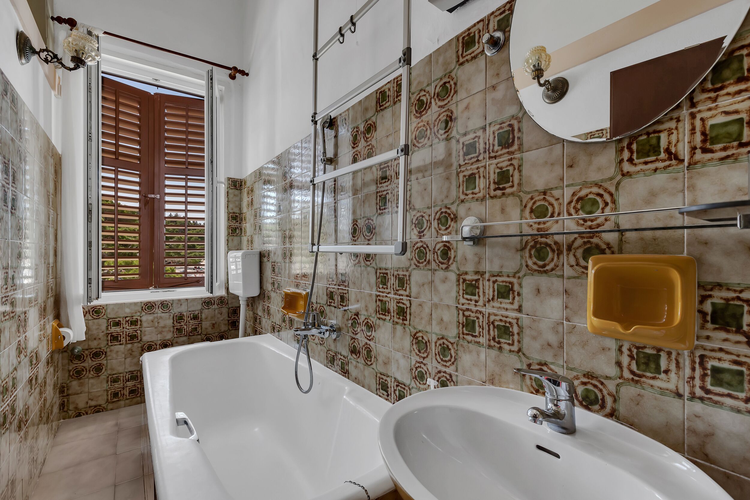 A bathroom with a large bathtub, a sink, and a window with wooden shutters.
