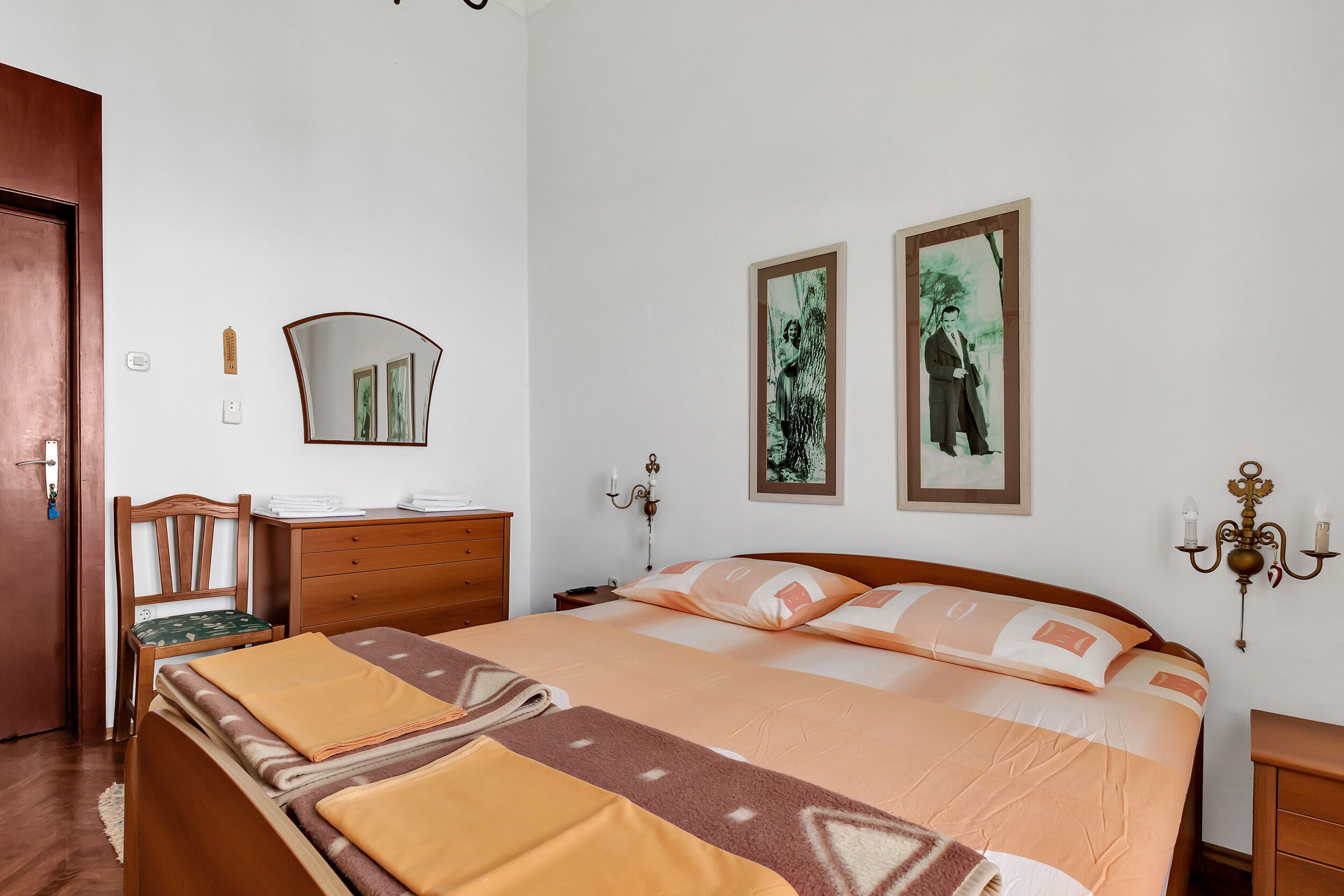 A neatly arranged bedroom with a bed, wooden furniture, a mirror, and two framed pictures on the wall.
