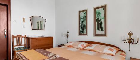 Un dormitorio ordenado con cama, muebles de madera, un espejo y dos cuadros en la pared.