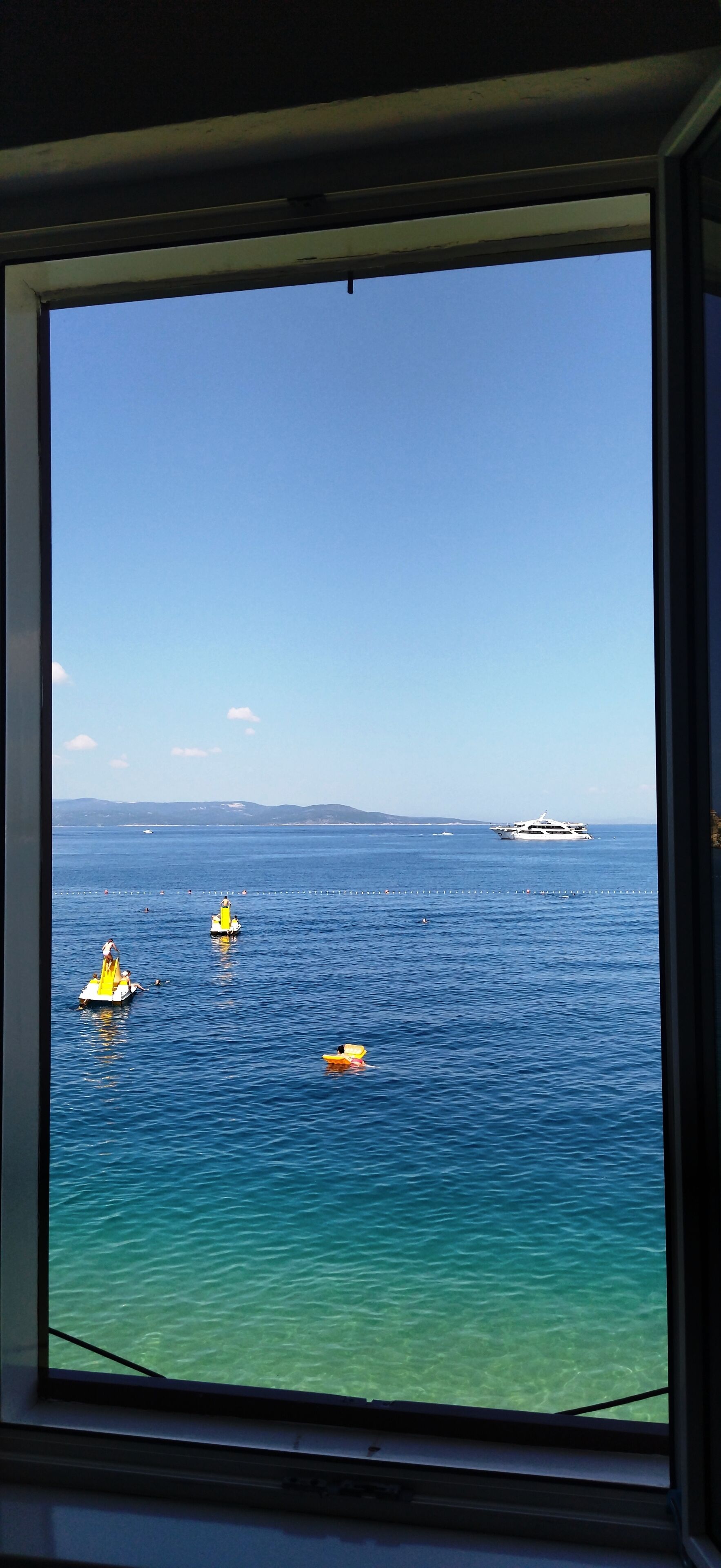 A view of the ocean through a window, with several boats visible on the water.