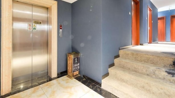 Een lift, een trap en een gang met blauwe wanden en houten deuren.