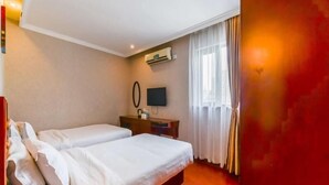 Een hotelkamer met twee bedden, een televisie, een bureau en een raam met gordijnen.