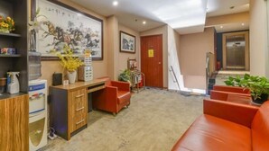 Een hotel lobby met een receptiebalie, een groot schilderij, een rode bank en een lift.
