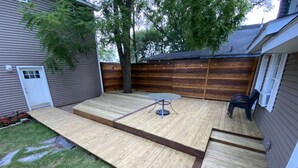 A backyard with a wooden deck, a round table, and chairs. - TC TWO OAKS Home / Minutes walk to Downtown & Beach (Traverse City)