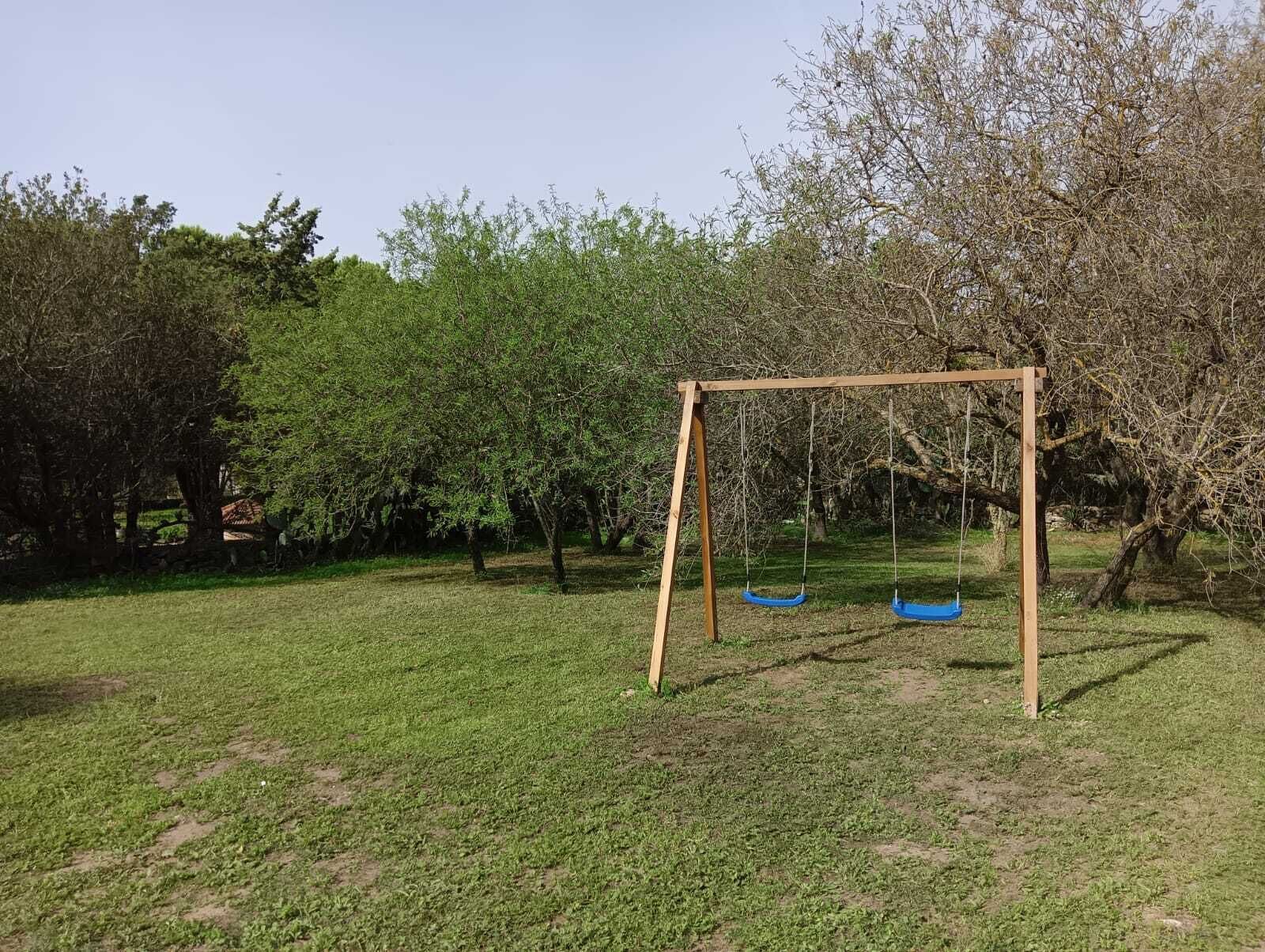 A wooden swing set in a grassy park area with trees in the background.