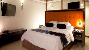 A neatly arranged bedroom with a large bed, a flat-screen TV mounted on the wall, and a bedside table with a lamp. - Nitro City Panama Action Sports Resort (Punta Chame)