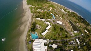 An aerial view of a coastal resort with a beach, a swimming pool, and several buildings. - Nitro City Panama Action Sports Resort (Punta Chame)