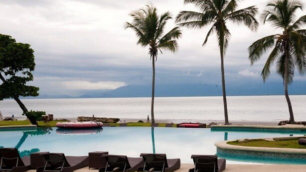 A pool with lounge chairs and palm trees, overlooking a body of water. - Nitro City Panama Action Sports Resort (Punta Chame)