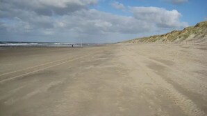 Een breed zandstrand met duinen aan de rechterkant en een heldere lucht.