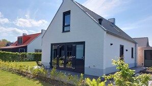 Een modern huis met een witte gevel, grote glazen deuren en een rood dak.