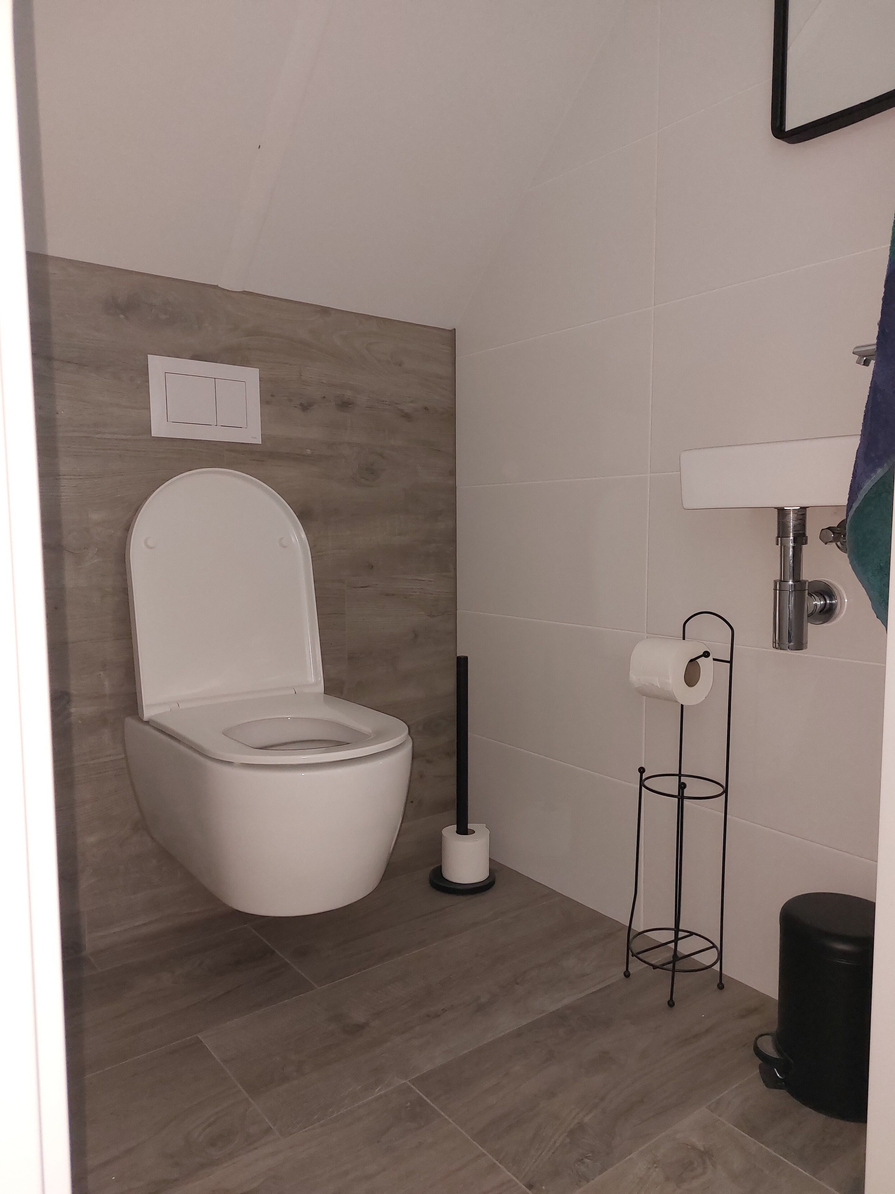 Uma casa de banho moderna com sanita, suporte para papel higiénico e um cesto de lixo.