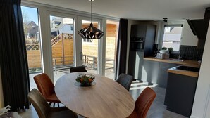 Een moderne keuken met een centraal eiland, een eethoek met een ronde tafel en stoelen, en grote ramen met uitzicht op buiten.