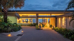 A modern building with a glass facade, a paved entrance, and tropical landscaping. - Ombak Luxury House- 5 bedroom Home / Concierge (Uvita)