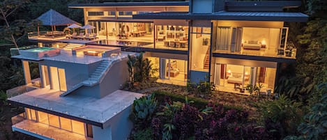 A modern multi-story house with a rooftop pool, large glass windows, and a well-maintained garden.