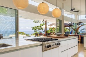 A modern kitchen with a large island, stainless steel appliances, and a view of the ocean.