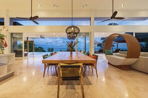 A spacious dining area with a long wooden table, multiple chairs, and a view of the ocean.