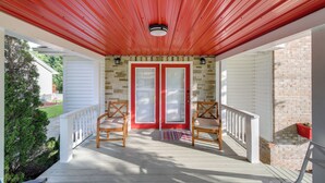 Een overdekt terras met een rood dak, twee houten stoelen, een witte balustrade en een bakstenen muur.