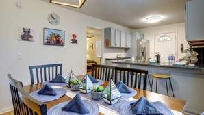 Een eethoek met een houten tafel, blauwe placemats en stoelen. Er liggen decoratieve kussens en er hangt een klok aan de muur.