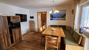 Une cuisine compacte avec des meubles en bois, un four à micro-ondes et un four encastré. On y trouve un coin repas avec une table et des chaises en bois, ainsi qu’un canapé près d’une fenêtre offrant une vue sur les montagnes.