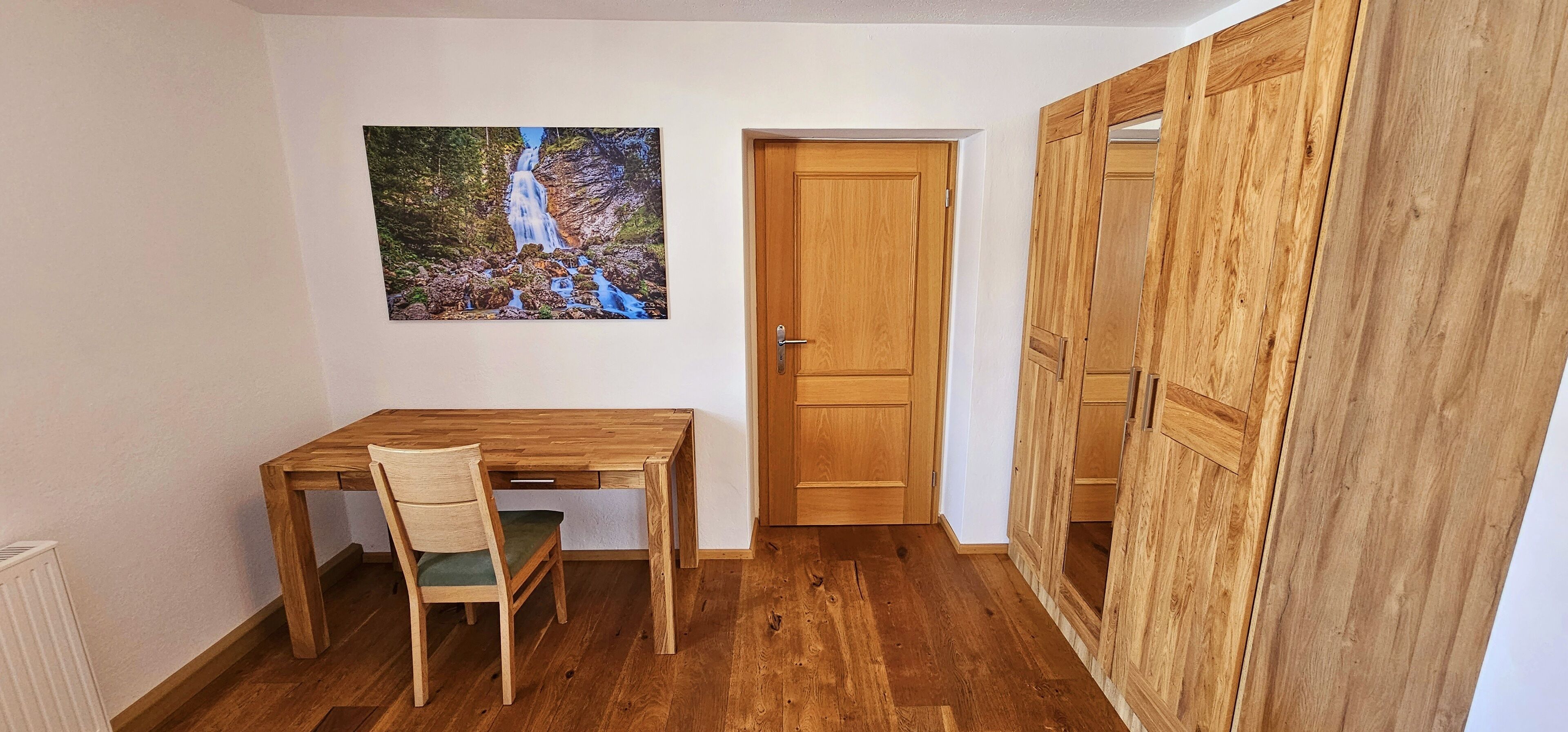 Una habitación con un escritorio de madera, una silla, un armario de madera y una puerta.