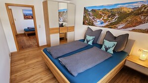 Une chambre à coucher avec un lit, une table de chevet, une lampe et un tableau représentant un paysage de montagne.