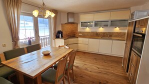Une cuisine compacte avec des meubles en bois, un four encastré et un coin repas comprenant une table en bois et des chaises à l’assise rembourrée de tissu vert.
