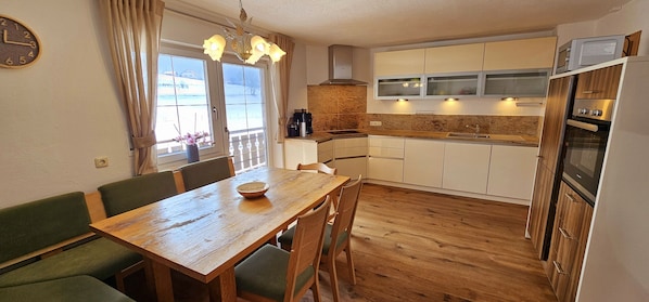 A compact kitchen with wooden cabinets, a built-in oven, and a dining area with a wooden table and green upholstered chairs.