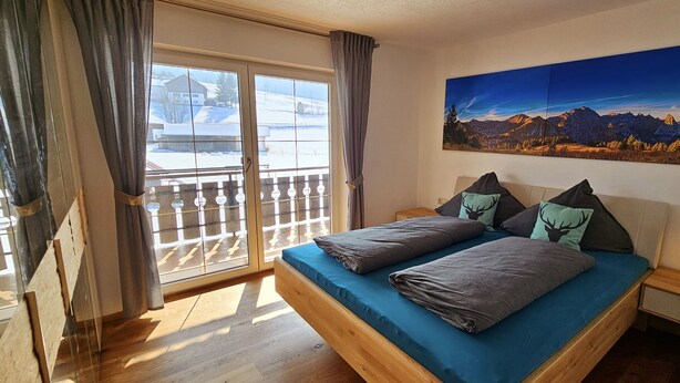 Une chambre à coucher avec un lit, une table de chevet, une lampe, un tableau et une vue sur les montagnes par la fenêtre.
