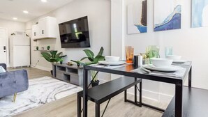 Una cocina moderna con armarios blancos, un televisor de pantalla plana y un comedor con mesa negra y banco.