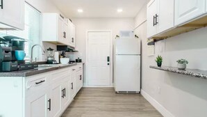 Una cocina estrecha con armarios blancos, un refrigerador blanco y una encimera con varios electrodomésticos.